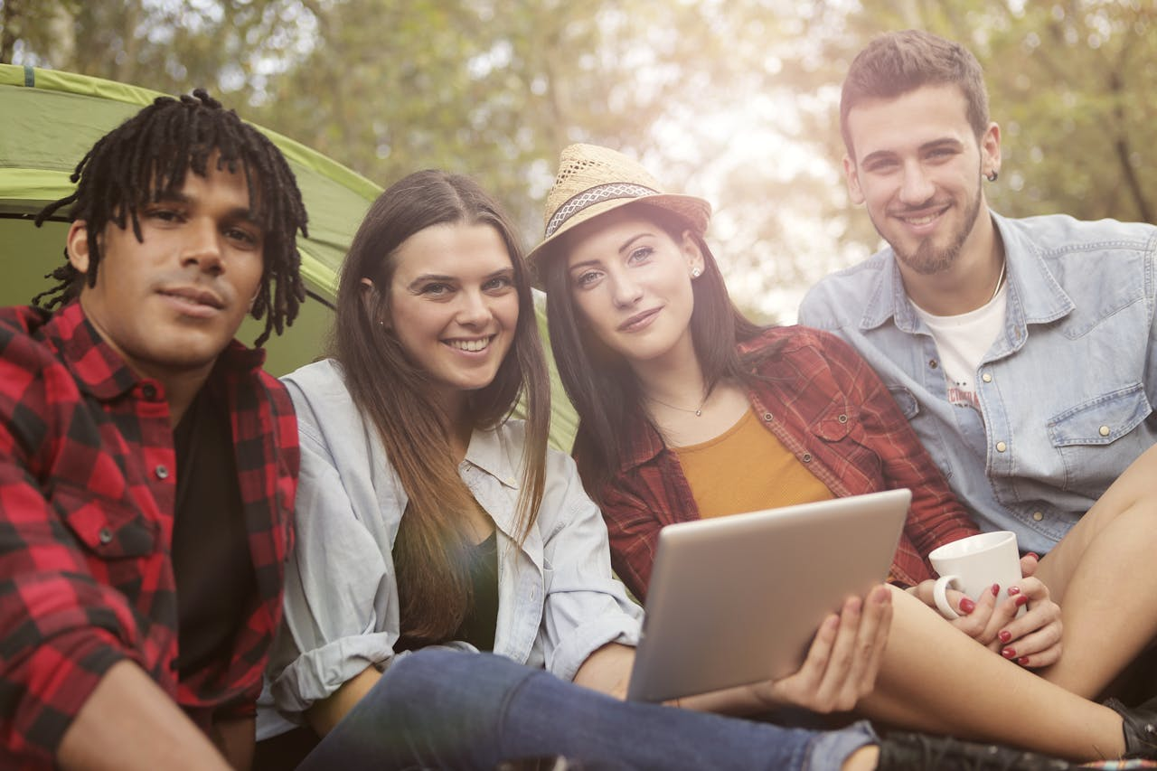 Four friends relaxing outdoors, enjoying a camping day with a tablet.
