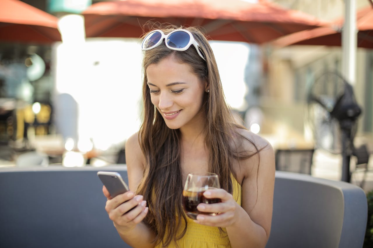 Smiling woman with a drink and smartphone outdoors enjoying leisure time happily.